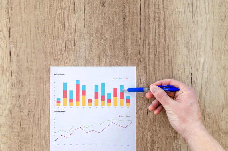 Hand pointing a pen at business performance graphs on a table